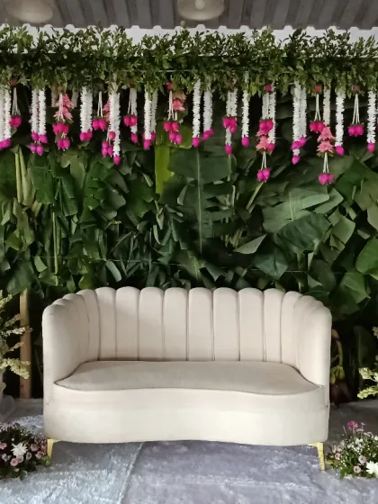 An elegant stage for your engagement ceremony. This design uses a lush green backdrop of banana leaves, accented with hanging floral arrangements and two large bouquets flanking a classic sofa for the happy couple.