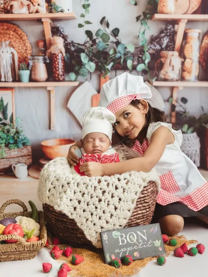 A protective hug for her sleeping baby brother. This sibling chef photoshoot is a beautiful way to capture their new bond.