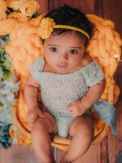 This little girl is perfectly posed in her basket, surrounded by a beautiful arrangement of yellow and blue flowers for her 3-month photoshoot.