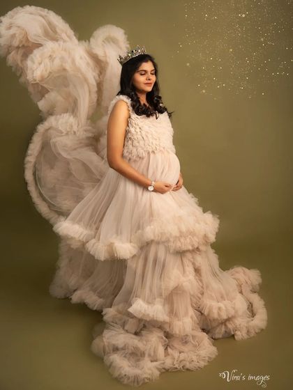 A truly angelic portrait. The mother-to-be, wearing a crown and a magnificent ruffled gown, looks serene as golden light dusts the air around her.