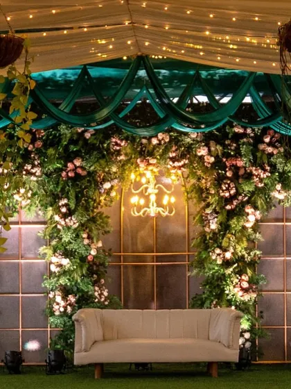 A lush green stage backdrop with a beautiful floral arrangement and an elegant chandelier, showcasing a classic and romantic decor theme.