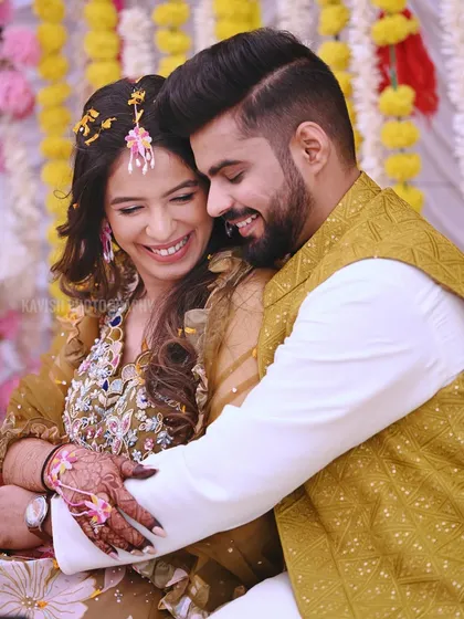 A heartwarming, candid embrace between a couple during their Haldi ceremony, surrounded by yellow floral decorations.