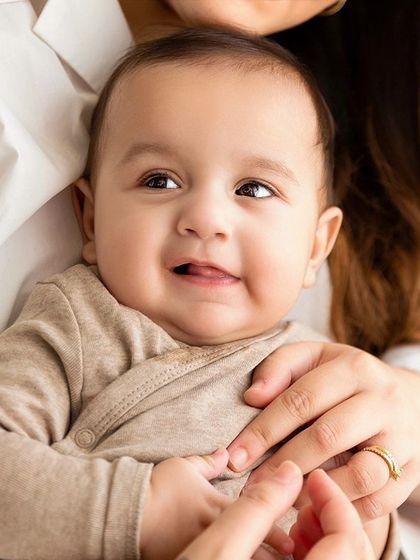 A close-up of a baby boy held in his mother's arms, looking up with a sweet expression.