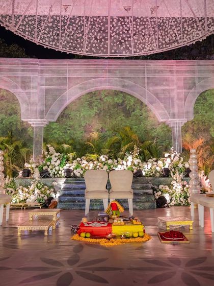 The mandap setup, featuring elegant seating for the couple against the stunning backdrop of greenery and white architectural elements. The design is clean, sophisticated, and deeply rooted in nature.