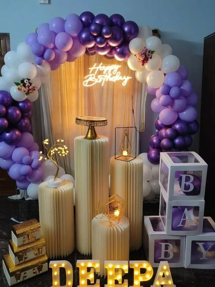 A simple yet elegant purple and white theme. This decoration uses a balloon arch, a neon sign, and 'BABY' display boxes, making it suitable for a baby shower or a first birthday.