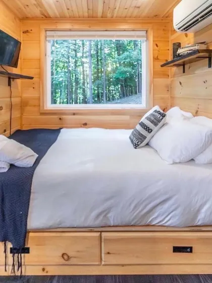 This container home bedroom is designed for efficiency and comfort. The built-in storage under the bed maximizes space, while the window provides a beautiful view of the natural surroundings.