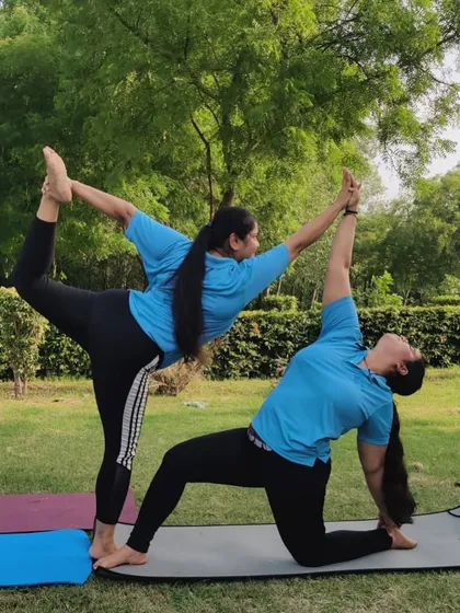 A graceful partner pose combining Natarajasana (Dancer's Pose) with a modified lunge, performed outdoors.