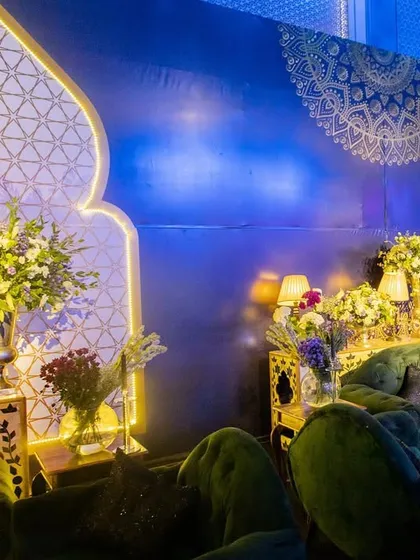 A luxurious lounge area for a Sangeet, with deep green velvet sofas and backlit panels in traditional motifs, creating a sophisticated and moody vibe.