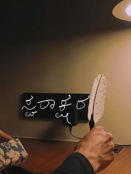Another shot from the 'Svarakshara' video, showing the song title written in Kannada on a modern desk setup. This blends traditional script with a contemporary aesthetic.