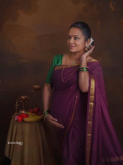 A graceful portrait of a mother-to-be in a traditional purple saree. She looks off to the side with a gentle smile, her hair adorned with flowers, in a classic, painterly style.