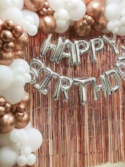 Another example of a birthday balloon decoration, this time with a mix of rose gold chrome and white balloons. The dense balloon garland frames the 'Happy Birthday' foil letters and the shimmery backdrop perfectly.