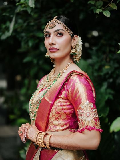 A close-up bridal portrait showcasing intricate jewelry and makeup. The natural green background makes the bride the absolute center of attention.