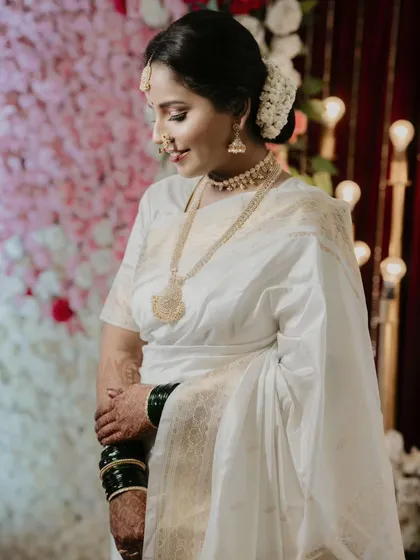 A candid portrait of the bride, Sayali, in her elegant white saree. The soft lighting and her gentle smile create a peaceful and beautiful image.