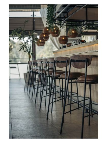 A line of sleek bar stools awaits guests, offering a prime view of the bar and the cityscape beyond. The design emphasizes clean lines and an uncluttered feel.