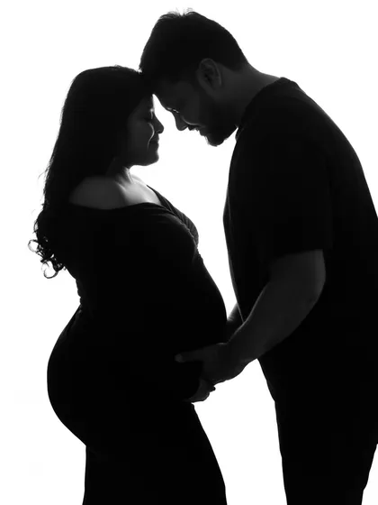 A dramatic and romantic silhouette of the couple. This black and white image captures their intimacy and the beautiful outline of the baby bump against a stark white background.