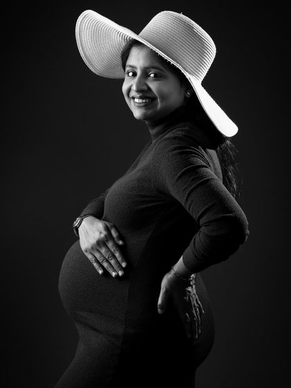 A chic and happy black and white portrait. The mom-to-be wears a stylish hat, adding a touch of glamour to this joyful and classic maternity photo.