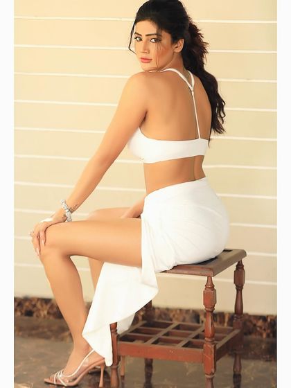 A simple and clean outdoor shot in a white two-piece outfit. The back-facing pose is elegant and highlights the design of the top and the model's posture.