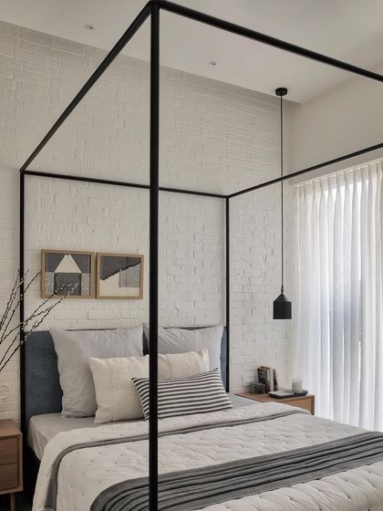 The daughter's love for white inspired this bedroom design. The four-poster bed is accentuated by a rustic white brick wall, while oak side tables add a touch of warmth and coziness, creating a dreamy and timeless space.