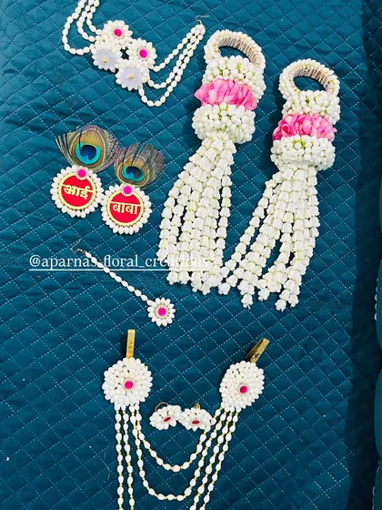 A unique baby shower jewellery set featuring 'Aai' and 'Baba' tags with peacock feathers. The set also includes bajuband with long tassels made of fresh flowers.