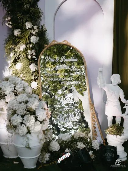 A personalized welcome sign for the couple, etched onto a gold-framed mirror and surrounded by abundant white flowers and classical statues.