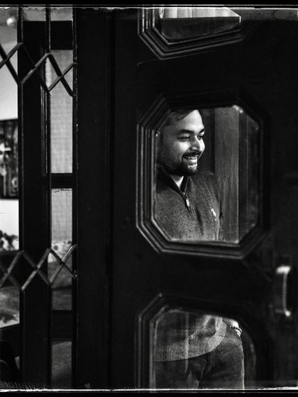 Yash, seen through the glass panels of a door. His smile is genuine, and the composition makes it feel like a private, happy moment.