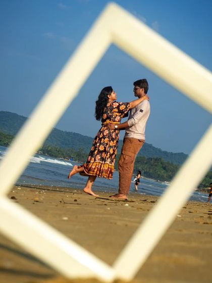 A series of creative pre-wedding photos using a frame as a prop. Here, the couple is captured in a romantic embrace, perfectly framed against the beach backdrop.