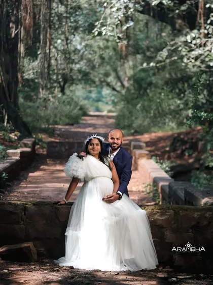 A stylish couple's maternity portrait in a forest. The mom-to-be looks radiant in a white gown with unique single-shoulder ruffles.