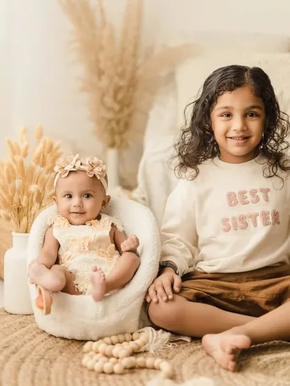 A proud big sister, wearing a "Best Sister" sweatshirt, sits next to her baby sister. This shot perfectly captures the sweet and protective sibling bond.
