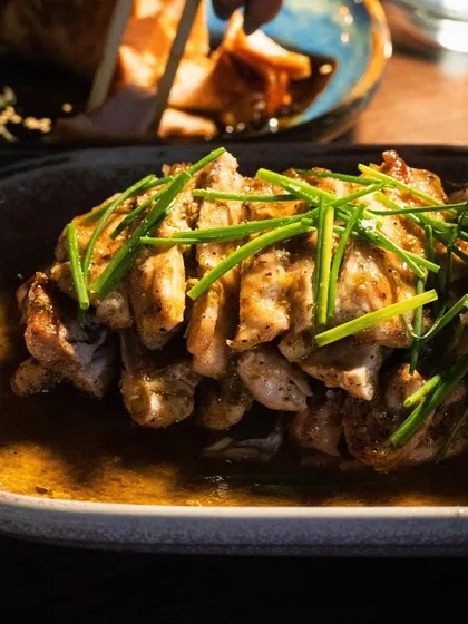 A plate of Chicken Anticucho, with the light catching the glistening sauce and fresh chives. The shot is warm and inviting.