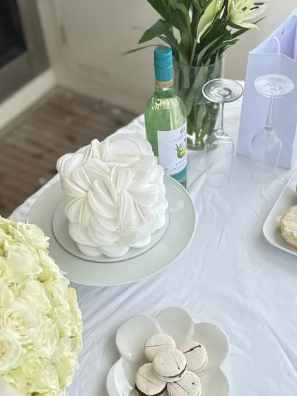 The perfect centerpiece for a chic, all-white party setup. This wafer paper bloom cake looks stunning alongside macarons and a crisp bottle of wine.