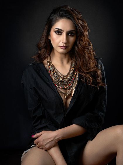 A moody studio portrait with a dark background. The lighting is focused on the model's face and the intricate statement necklace, creating a sense of intimacy and intensity.