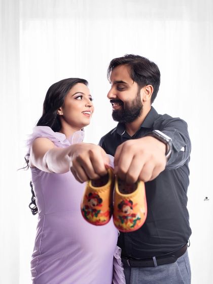 A classic and happy couple's announcement photo. They hold up a pair of tiny shoes together, symbolizing the new life they are about to welcome.