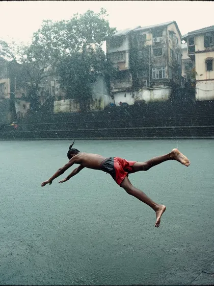 A boy in mid-air, diving into the waters of Banganga Tank during a rainstorm. This action shot captures the energy and tradition of this unique location, where the monsoon is a time for celebration and play.