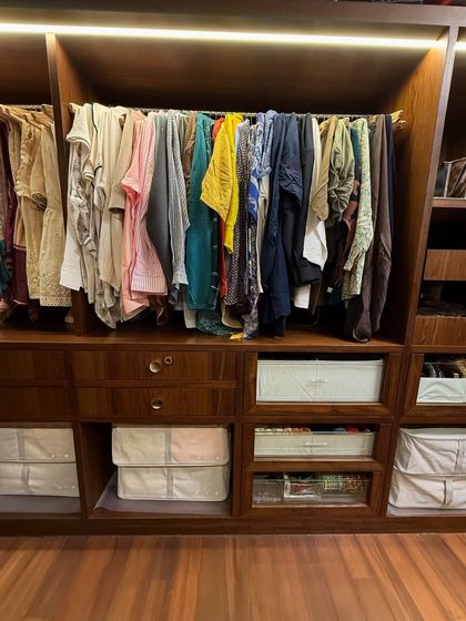 A well-organized closet section featuring hanging clothes, open shelving with bins, and drawers, all within a rich, dark wood finish.