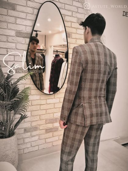 A back view of the plaid double-breasted suit, showing the clean lines and perfect fit. The mirror reflection gives a glimpse of the front profile.