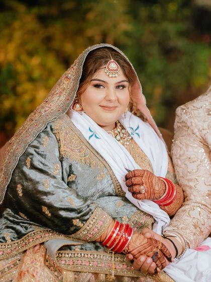 A serene portrait of a bride. The dark henna on her hands provides a beautiful, traditional contrast to her elegant wedding outfit.