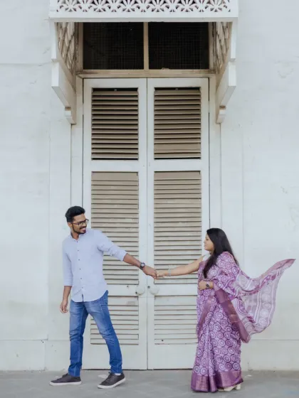 A stylish pre-wedding photo of the couple in front of a grand white door, creating a clean and elegant composition.