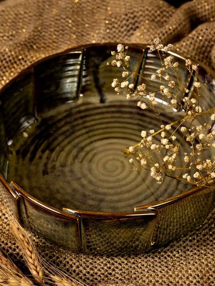 The empty ceramic bowl is styled with dried wheat and baby's breath on a rustic jute surface. This composition highlights the bowl's earthy texture and the beautiful spiral pattern on its interior.