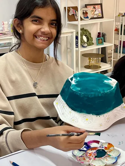 A smiling teenager shows off the daisy-themed bucket hat she's painting at a friend's birthday party.