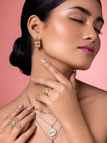 A close-up on the details: the texture of the gold earrings and rings, and the flawless, glowing skin.