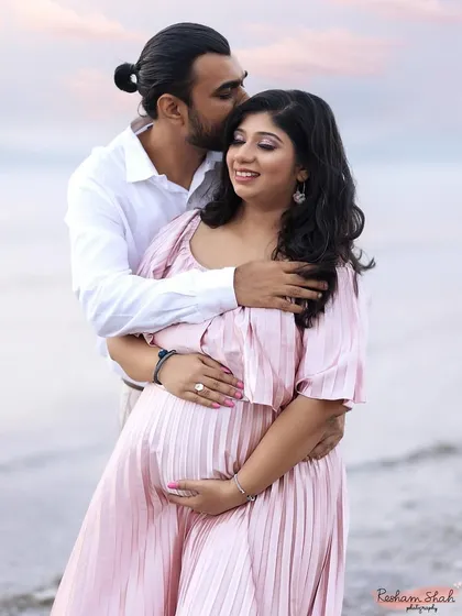 An affectionate embrace captured by the sea. The dad-to-be wraps his arms around his partner and kisses her temple, a perfect picture of love and anticipation.