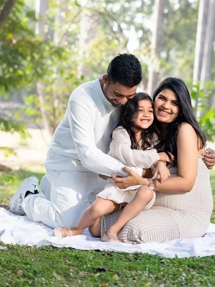Love grows here. A beautiful family shares a warm hug in a sunlit park during their outdoor maternity session, celebrating the upcoming arrival of their new baby.