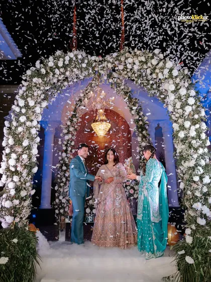 The couple celebrates their union under a shower of confetti, framed by a magnificent floral arch. This shot captures the peak excitement of an engagement party.