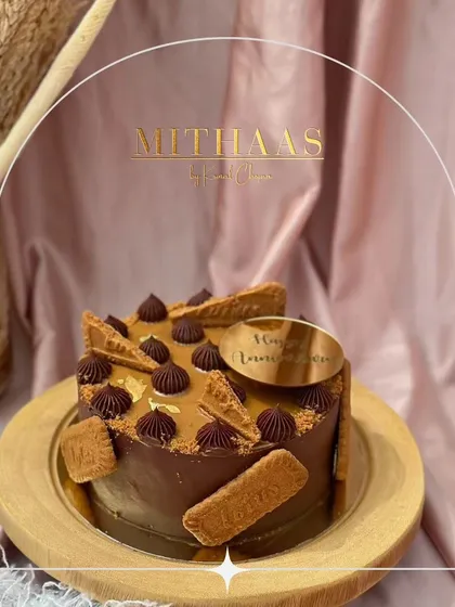 A round Lotus Biscoff and chocolate cake, perfect for an anniversary. The design features Biscoff biscuits, piped chocolate details, and a custom "Happy Anniversary" topper.