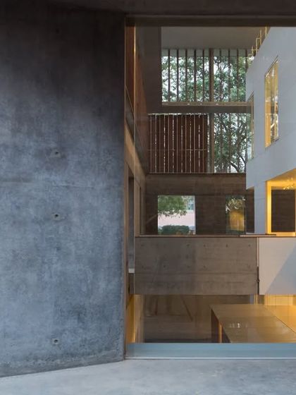 A view through an opening in a concrete wall at the Lilavati Lalbhai Library reveals the complex, multi-layered interior. This framing device creates a sense of depth and invites exploration of the spaces within.