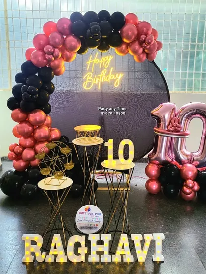 A stylish 10th birthday party for Raghavi with a red chrome and black balloon arch. The setup includes a custom backdrop, foil number balloons, and light-up name letters.