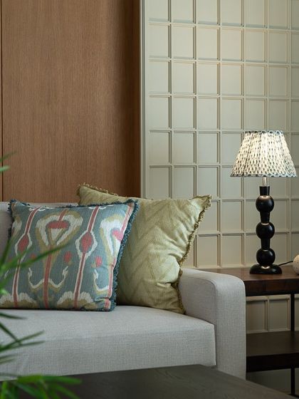 Another cozy corner, where a textured lamp and patterned cushions add personality to a neutral sofa. The gridded wall paneling provides a subtle geometric backdrop.