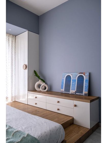 This daughter's bedroom is given a pop of color with a periwinkle blue wall and a fun C-shaped wooden platform bed. The design includes tall storage and a drawer unit that doubles as a sitting bench.
