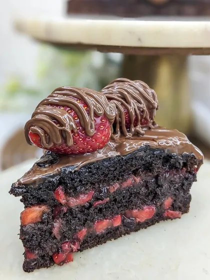 A close-up of a slice of our Boozy Nutella Strawberry cake. The layers are soaked in rum, adding a warm kick to the classic chocolate and strawberry combination.