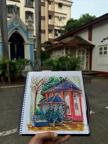 Holding up my colorful sketch of a beautiful old house in Ranwar village, Bandra. This image shows how I use acrylic markers to capture the unique character and charm of Mumbai's hidden gems, with the real-life inspiration right there in the background.